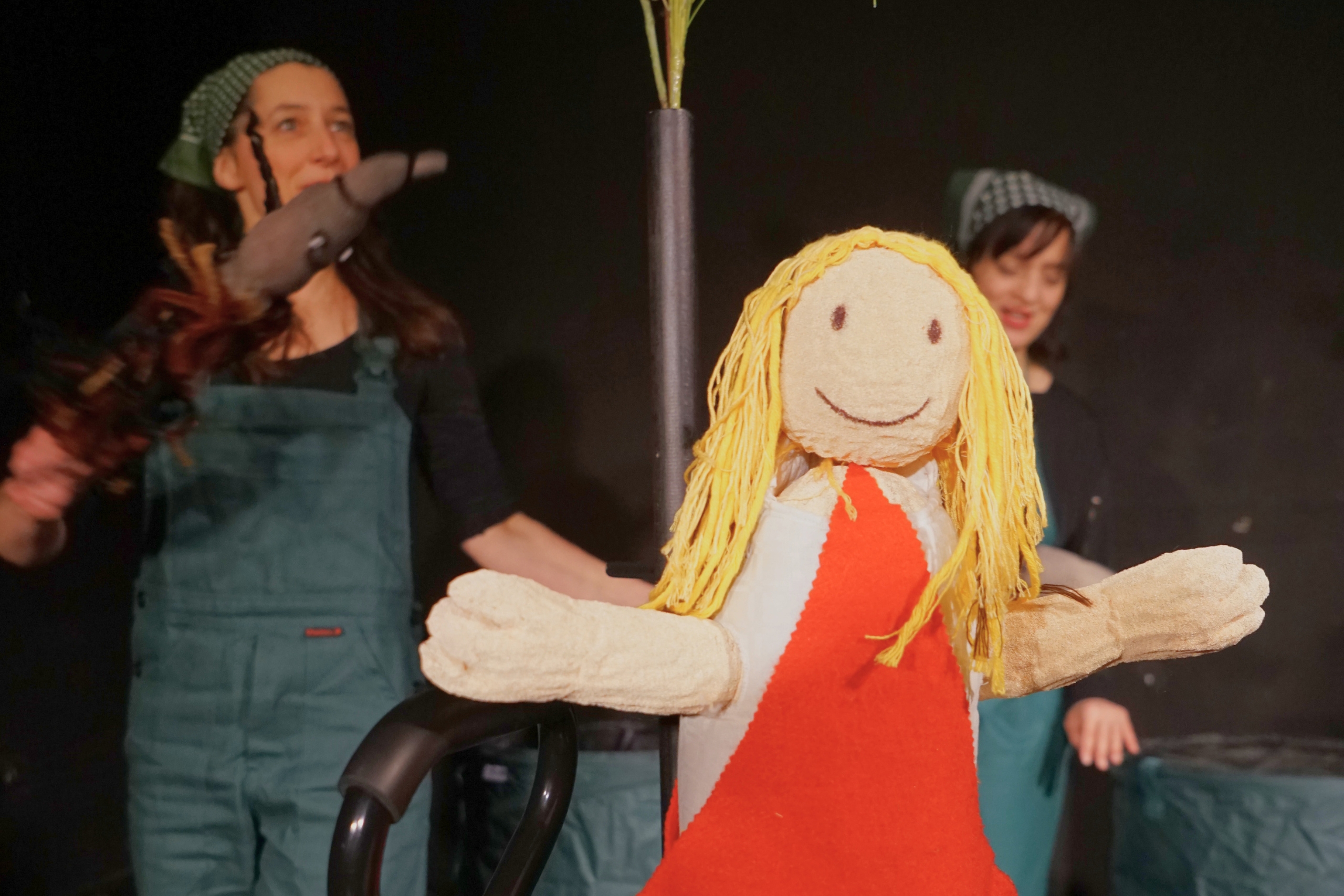 Däumelinchen Puppe im Vordergrund. Im HIntergrund zwei verkleidete Frauen, die ein Theaterstück spielen.