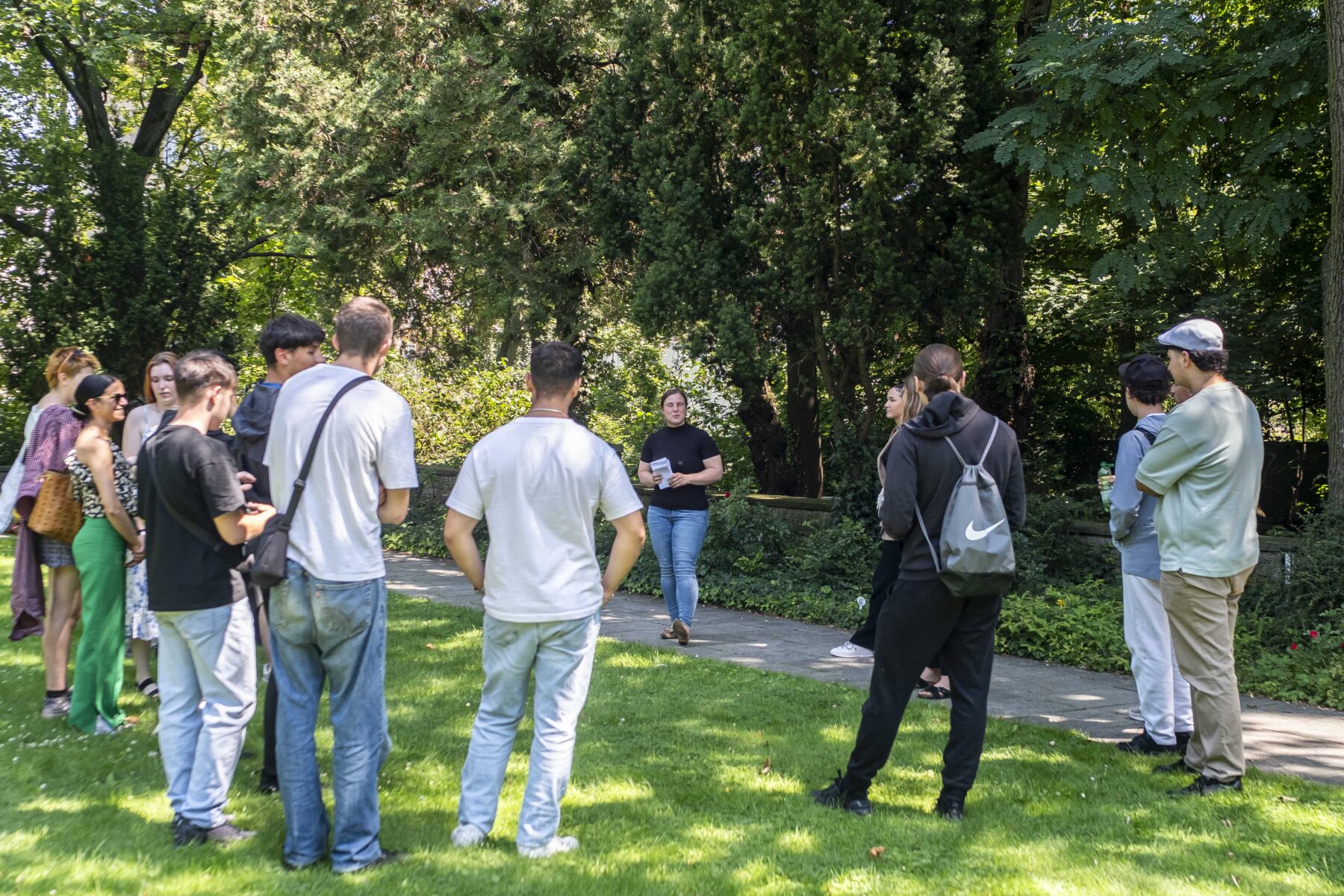 Eine Gruppe von Menschen im Kreis stehend. Eine Frau gibt eine Führung.